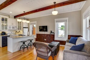 A spacious kitchen with a central island, bar stools, a dining table, and a living area with a sofa and a television.