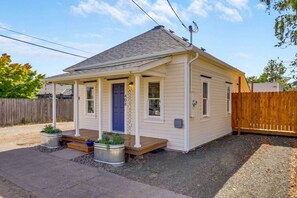Ein eingeschossiges Haus mit Veranda, einer blauen Tür und einem kleinen Garten mit Blumentöpfen.