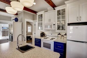 A kitchen with white cabinets, a stainless steel sink, a white refrigerator, and a stove.