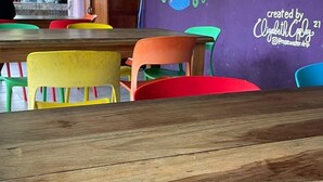 A wooden table in a room with colorful chairs, a purple wall with a mural, and a ceiling fan. - Planet B Hostel (Quepos)