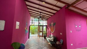 A hallway with pink walls, a green sofa, and a book exchange sign. - Planet B Hostel (Quepos)