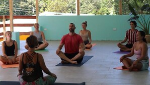 A group of people seated on yoga mats in a room with a tiled floor and a light-colored wall. - Planet B Hostel (Quepos)