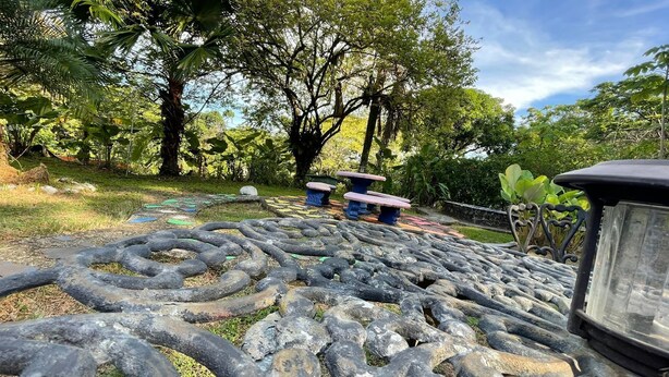 A garden with a stone pathway, a metal sculpture, and a bench. - Planet B Hostel (Quepos)