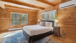 Un dormitorio de cabaña de madera con una cama, mesitas de noche y una ventana.