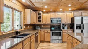Una cocina moderna con armarios de madera, electrodomésticos de acero inoxidable, encimeras de granito y techo de madera.