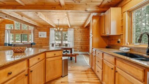 Interior de una cabaña de madera con cocina, comedor y un amplio ventanal.