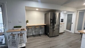 Una cucina moderna con un frigorifero in acciaio inossidabile, sgabelli da bar in legno e un piano di lavoro bianco.