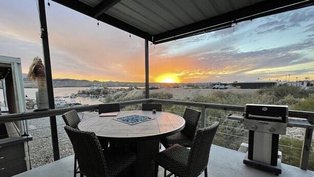 Una veranda coperta con un tavolo rotondo e sedie, un barbecue e vista su un tramonto nel paesaggio desertico.