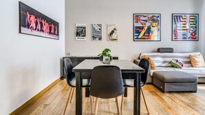 Ein modernes Wohnzimmer mit Esstisch, Stühlen, einer Couch und einem Bett. Vier gerahmte Kunstwerke hängen an der Wand.