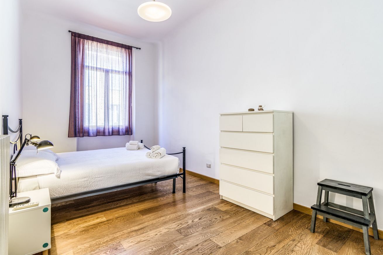 Ein Schlafzimmer mit Bett, Schrank, Nachttisch und einem Fenster mit Vorhängen.