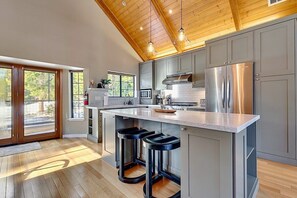 A modern kitchen with a large island, stainless steel appliances, and a wooden ceiling.