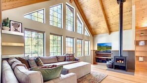 A spacious living room with a large sectional sofa, multiple windows, a fireplace, and wooden beams on the ceiling. - Private Ski, Lake & Golf Chalet! Walk to Lake (Tahoe Vista)