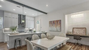 A modern kitchen with white cabinetry, a central island, and a dining area with a white table and chairs. - 30A Treetop Retreat • Shared Pool + Private Beach Access + Bikes | Pura Vida (Seacrest Beach)