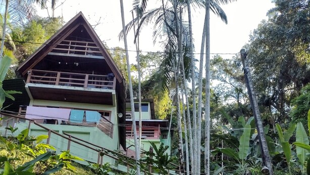 A rustic house with a sloped roof, surrounded by lush greenery and a stone staircase leading up to it. - Beautiful chalet with panoramic views (Ubatuba)