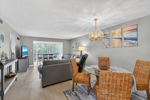 A modern living room with a grey sofa, wicker chairs, a glass coffee table, and a television. - 2 Bed 2 Bath Centrally Located (Siesta Key)