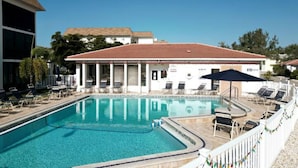 A swimming pool with lounge chairs and umbrellas, surrounded by a building with a tiled roof.
