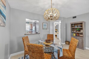 A dining area with a glass table, wicker chairs, a decorative hanging light fixture, and a bookshelf with various items. - 2 Bed 2 Bath Centrally Located (Siesta Key)