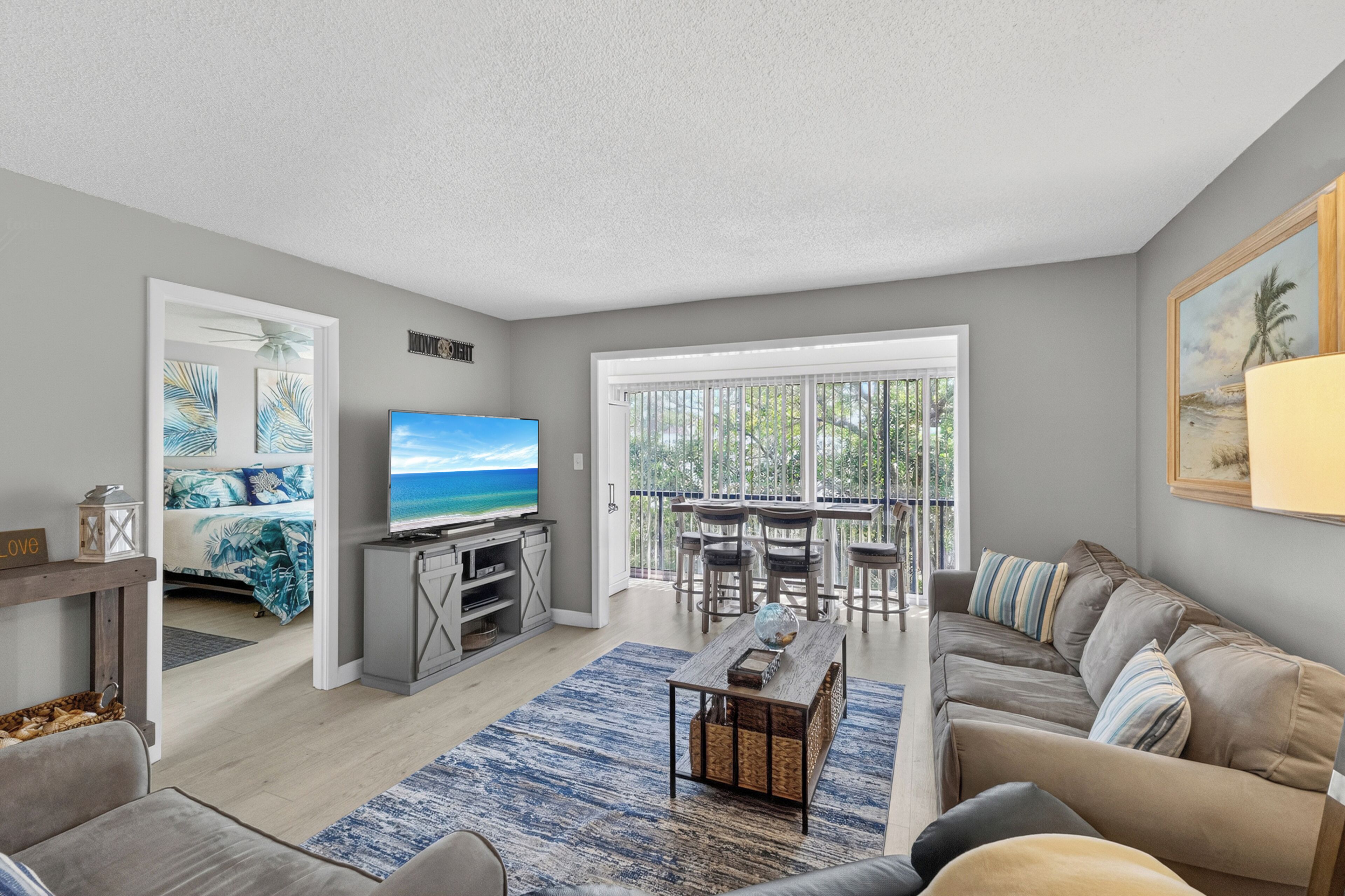 A modern living room with a flat-screen TV, a sofa, a coffee table, and a dining area with chairs and a table.