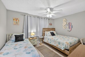 A bedroom with two beds, a ceiling fan, a nightstand with a lamp, and decorative wall art.