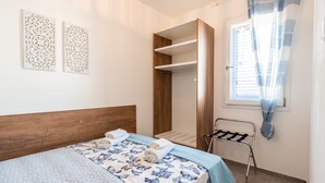 A bedroom with a bed, a wooden wardrobe, a drying rack, and two wall decorations. - VILLINO LORENZO for Rent 3 min from Porto Cesareo with Pool (Boncore)