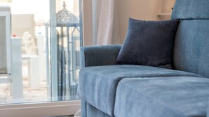 A modern living room with a grey sofa, a large window, and a view of a building outside. - VILLINO LORENZO for Rent 3 min from Porto Cesareo with Pool (Boncore)