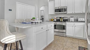 A modern kitchen with white cabinetry, a marble countertop, and stainless steel appliances. - Melbourne Beach House (West Melbourne)