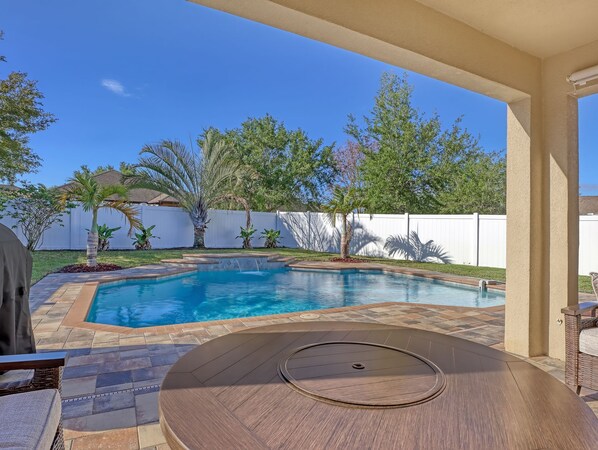 A backyard with a swimming pool, a covered patio table, and a white fence.