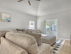 A spacious living room with a large sectional sofa, a small ottoman, and a ceiling fan. There is a sliding glass door leading to a patio area.