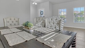A dining area with a dark wooden table, light-colored chairs, and a potted plant. - Melbourne Beach House (West Melbourne)