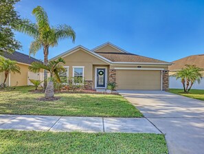A single-story house with a beige exterior, a garage, and a front yard with palm trees and a well-maintained lawn.