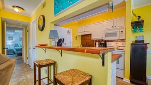 Una cucina con pareti gialle, mobili bianchi e un bancone bar in legno. Sono presenti due sgabelli in vimini e un forno a microonde.
