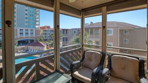Un balcone con mobili in vimini, una piscina e vista sugli edifici circostanti.