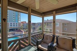 A balcony with wicker furniture, a pool, and a view of surrounding buildings.