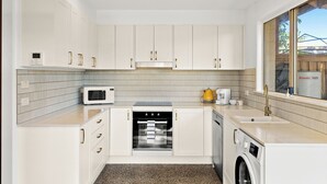 Een moderne keuken met witte kasten, een magnetron, een oven, een koffiezetapparaat en een wasmachine.