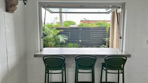 Een kleine keuken met een raam, twee groene stoelen en een wit aanrecht.
