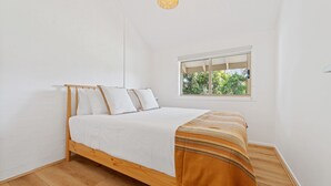 Een slaapkamer met een houten bed, wit beddengoed, een raam met uitzicht op groen en een hanglamp.