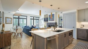A modern kitchen with a central island, dining area with a sofa, and a large window.