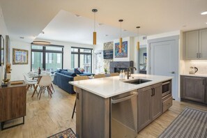 A modern kitchen with a central island, dining area with a sofa, and a large window.