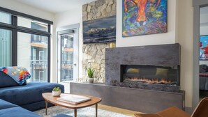 A modern living room with a fireplace, a sofa, a coffee table, and a painting on the wall.