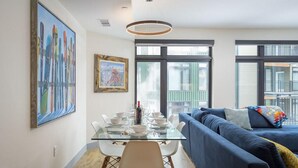 A modern living room with a glass dining table, blue sofa, and large windows.