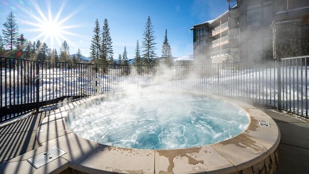 A hot tub surrounded by a metal fence, with snow on the ground and trees in the background.