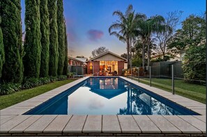 Uma piscina retangular com superfície de água azul cristalina, rodeada por um deck pavimentado.