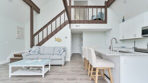 A modern living space with a staircase, a sofa, a coffee table, a dining area, and a kitchen. - 5260-Shenanigan's, 3BR Soundfront Home | Gated Community Pool (Kill Devil Hills)