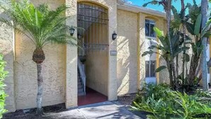 A building with a textured facade, a barred entrance, and a small staircase leading to a red-carpeted area. - Lovely 3 Bedroom Condo On Golf Course (Sarasota)
