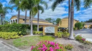 A hotel entrance with a sign, palm trees, and well-maintained landscaping. - Lovely 3 Bedroom Condo On Golf Course (Sarasota)