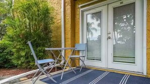 A door with a number "100" above it, a blue mat with white lines, and a small table with two chairs outside. - Lovely 3 Bedroom Condo On Golf Course (Sarasota)