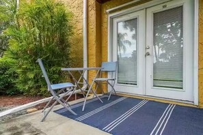 A door with a number "100" above it, a blue mat with white lines, and a small table with two chairs outside.