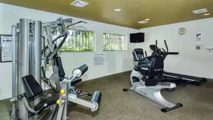 A gym with cardio and strength equipment, a TV, and windows with bars. - Lovely 3 Bedroom Condo On Golf Course (Sarasota)