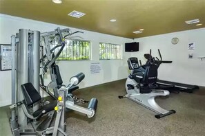 A gym with cardio and strength equipment, a TV, and windows with bars.