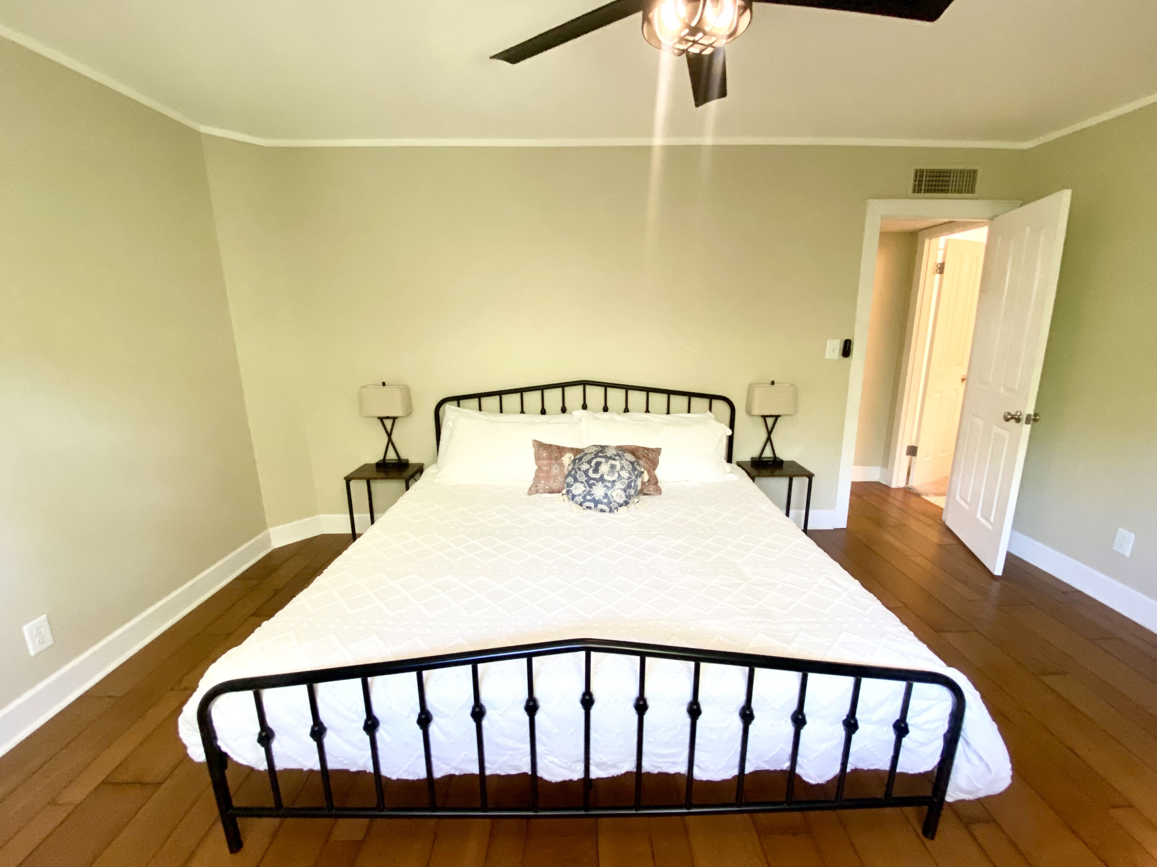 A bedroom with a bed, two bedside tables, a ceiling fan, and a door leading to another room.
